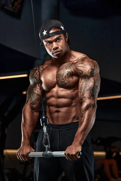Homme afro-américain fort et musclé s'entraîne sur des équipements modernes dans la salle de gym. Portrait de musclé pompé entraîneur de conditionnement physique — Photo