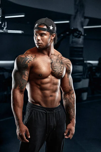 Homme afro-américain fort et musclé s'entraîne sur des équipements modernes dans la salle de gym. Portrait de musclé pompé entraîneur de conditionnement physique — Photo