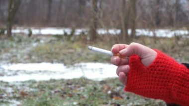 Eldivenler kırmızı, sigaralar tutuşsun. Sigara dumanı arka planda bulanıklaştı. Soğuk hava. Arka planda kar ve ağaçlar yumuşak odak.