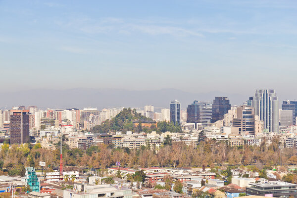 Santiago cityview from Cerro San Cristobal. Buldings and cerro Santa Lucia can be seen in front of moutains and blue sky. Pollution is present too.