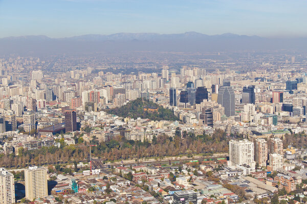 Santiago cityview from Cerro San Cristobal. Buldings and cerro Santa Lucia can be seen in front of moutains and blue sky. Pollution is present too.