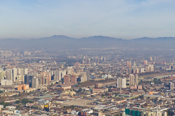 Santiago cityview from Cerro San Cristobal. Buldings can be seen in front of moutains and blue sky. Pollution is present too.
