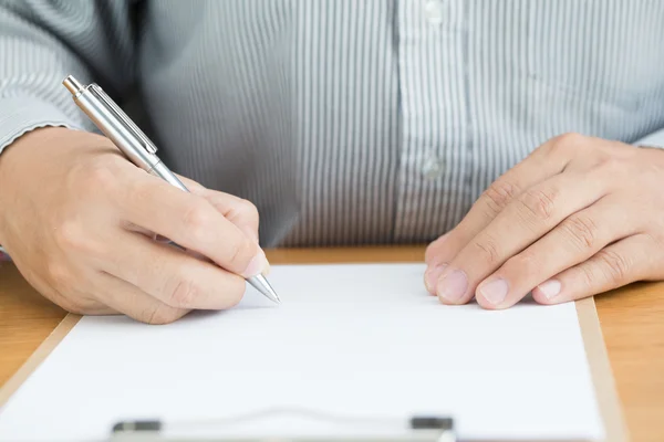 Human hand signing white paper on wood table — Stock Photo, Image
