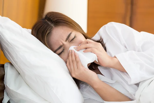 Asian woman sneezing in a tissue on bed — Stock Photo, Image