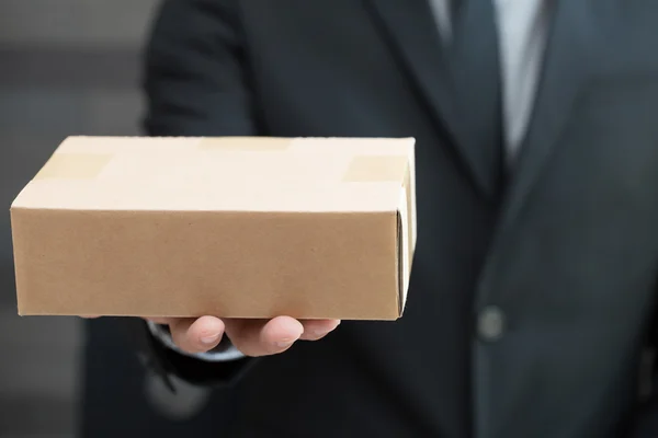 Бизнесмен в костюме дает кому-то коричневую коробку — стоковое фото