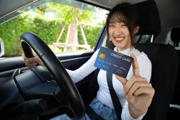 Happy young Asian woman driver holding payment card, member card, credit card and sitting in ca