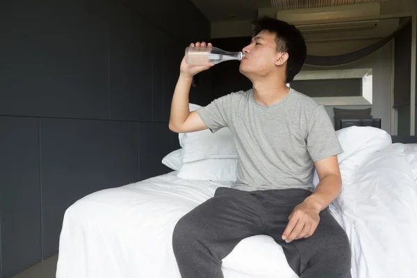 Pitná voda. Asijský mladík pitné vody na posteli — Stock fotografie