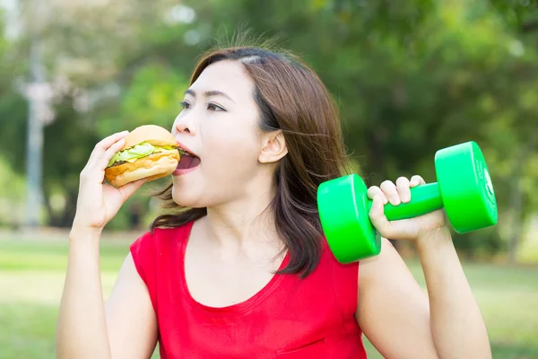 Mulher asiática comendo hambúrguer com levantamento de peso — Fotografia de Stock