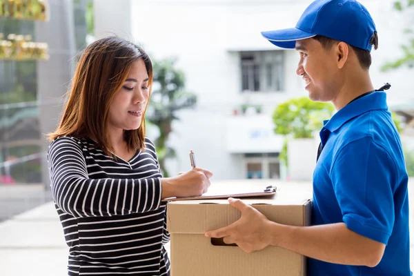 Mulher asiática que assina o recibo do pacote entregue — Fotografia de Stock