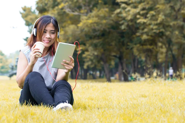 Mujer asiática escuchar música en la tableta y sosteniendo vaso de café i —  Fotos de Stock