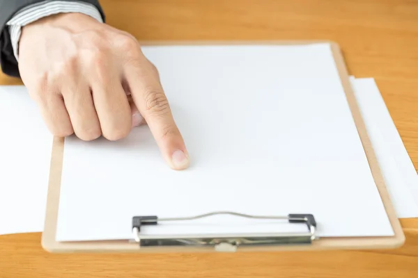 Рука бизнесмена указывает белой бумагой на деревянный стол — стоковое фото