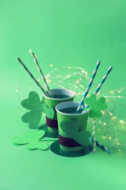 Kamış, yonca ve yeşil arka plan aydınlatma ile Aziz Patrick şapkası şeklinde kağıt bardaklarda iç, parti, tebrik, kartpostal