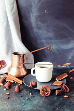 Sıcak kahve, bakır kahve makinesi, masada çikolata ve baharatlar, koyu arka plan, ev mutfağı.