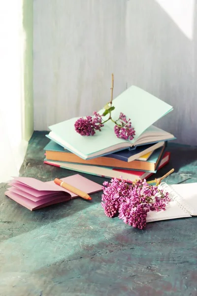 Books, notepads and fresh lilac flowers on table by the window, home schooling concept, back to school