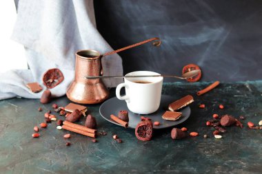 Sıcak kahve, bakır kahve makinesi, masada çikolata ve baharatlar, koyu arka plan, ev mutfağı.