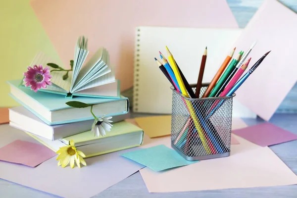 Books with bookmarks of flowers, pencils, notepads on the table, on a background of colored paper of pastel colors, the concept of learning, education, back to school