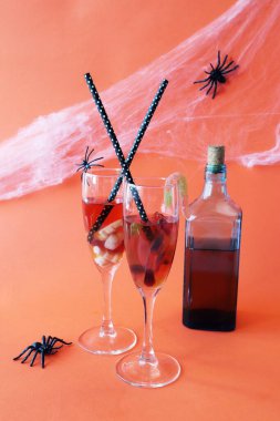 Cadılar Bayramı içkileri, solucanlı kırmızı şarap ve dişler, balkabakları, örümcekler ve turuncu arka planda mistik süslemeler.
