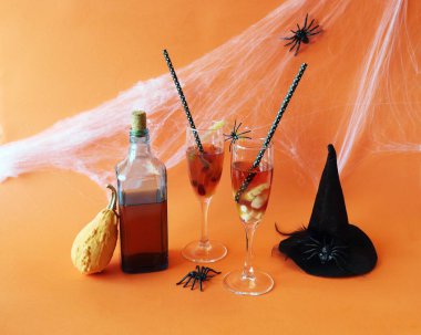 Cadılar Bayramı içkileri, solucanlı kırmızı şarap ve dişler, balkabakları, örümcekler ve turuncu arka planda mistik süslemeler.