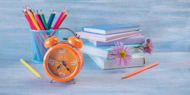 Okula dönelim. Kitaplar ve renkli kalemler, bir çalar saat ve ahşap bir masanın üzerindeki çiçek yer imleri. Ders çalışma zamanı. Kavram.