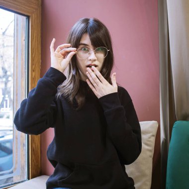 Gözlüklü genç kadın beklenmedik bir şeye tepki veriyor. Bir kadında şaşkınlık hissi, kafenin içinde..