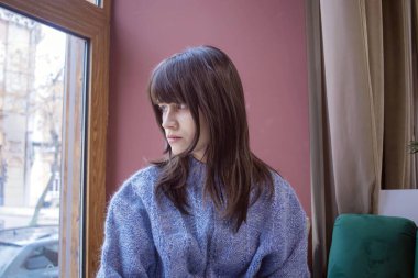 Pencerenin kenarında rahat bir kazak giymiş düşünceli bir kadın.