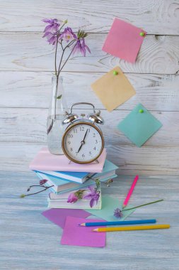 Kitaplar, çiçekler ve çalar saatle dolu bir masa. Okul malzemeleri ve bahar çiçekleriyle dolu bir hayat, okula dönmek..