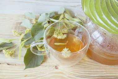 Cam bardakta ıhlamur çayı, taze ıhlamur çiçekleri, ahşap bir arka planda. Şifalı bitki çayı..