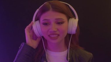 Mutlu gülümseyen Asyalı kız modern müzik dinle, kulaklık tak neon ışıkta