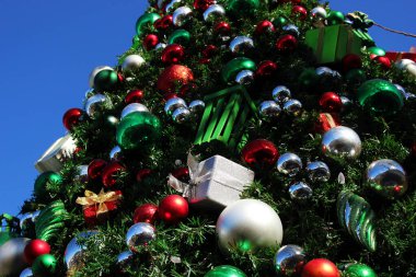 Toplar ve hediyeler şeklinde oyuncaklarla süslenmiş Noel ağacı. Mavi kış gökyüzüne karşı Noel ağacı. Noel oyuncağı.