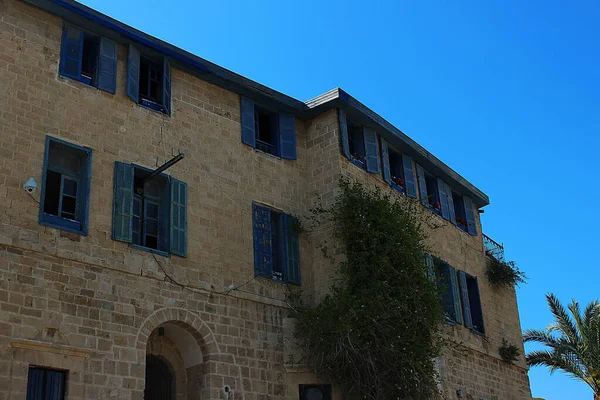 Evin ön cephesinde mavi ahşap panjurlu pencereler sarı İsrail taşından yapılmıştır. Pencereleri ve mavi gökyüzüne karşı bir palmiye ağacı olan bir yerleşim yeri. Tel Aviv - Jaffa, İsrail.