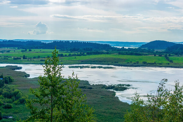 Summer pastoral landscape with forest, calm river and low mountains