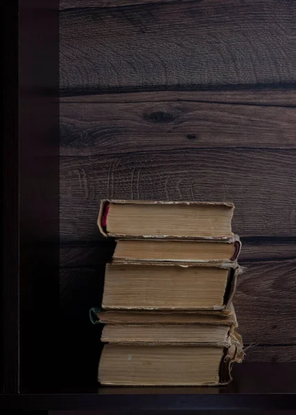 Stack of old paper books on dark shelf, vertical image