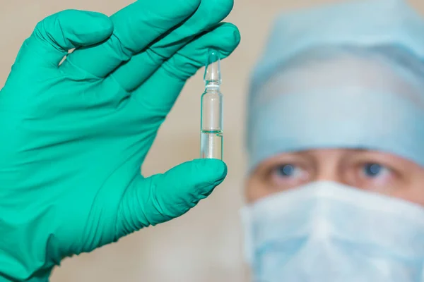 Man in doctor's cap and mask holds in sterile glove a ampoule with a remedy