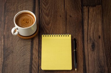 Aroma fincan kahve, boş not defteri ve tahta masa üzerindeki kalem.