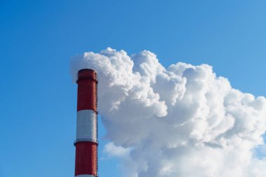 Mavi gökyüzündeki endüstriyel bacadan beyaz duman dökülüyor.