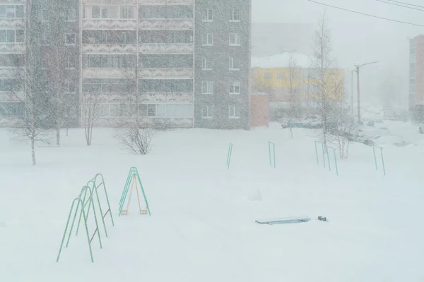 A yard in a neighborhood with apartment buildings at snow storm in winter