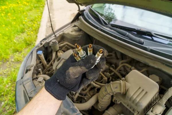 Hand with spark plugs while checking ignition system and replacing spark plugs