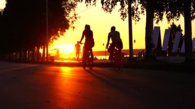 Gün batımında Rusya 'nın Petrozavodsk kentindeki göllerde yavaş çekimde bisikletçilerin ve aylakların siluetleri.