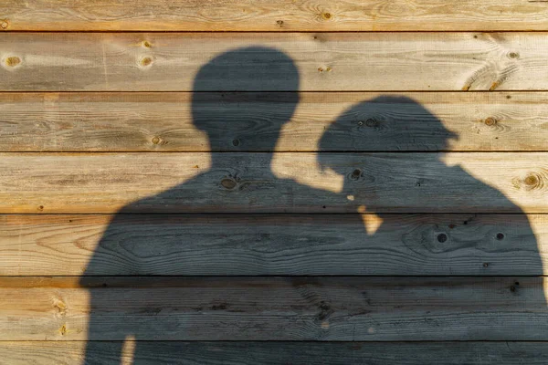 Shadow of man and woman on rustic wooden wall on sunny evening