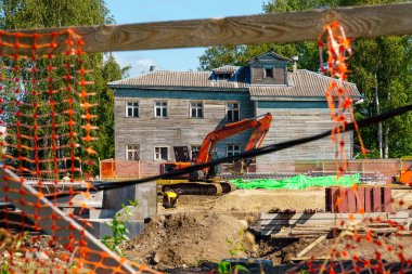 Çitteki bir delikten geçen kazıcıyla birlikte şehirdeki inşaat alanının görüntüsü