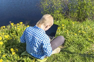 Ten year boy with laptop on riverside in summer
