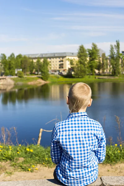 Ten year boy looks on city from river shore — Stockfoto