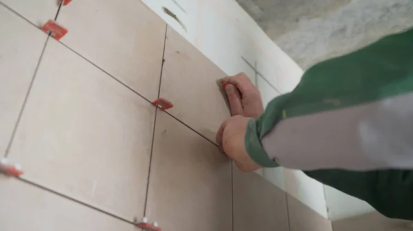 Master in overalls puts ceramic tiles on the wall. The master puts the tiles in the bathrooms.