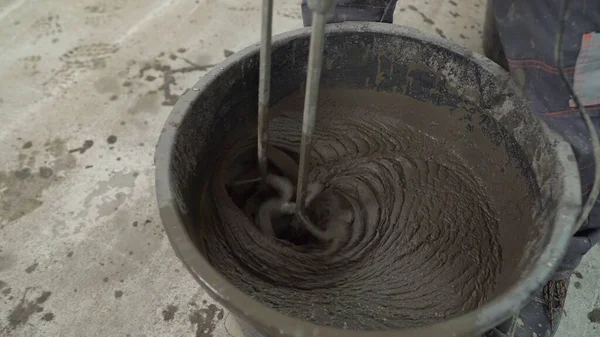 A bucket of solution is mixed in a bucket close-up. The drill nozzle is inserted into wet cement. Wet mortar mixture for finishing work in construction. Traces of tool rotation. Repair in the household. Close-up, selective focus.