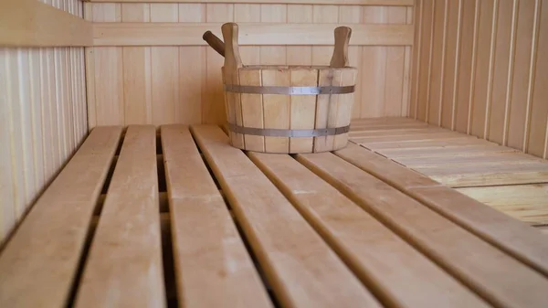 Wooden bucket in the interiors of the bath. Sauna room with traditional sauna accessories for healthy. Vennik and wooden bucket in the sauna.