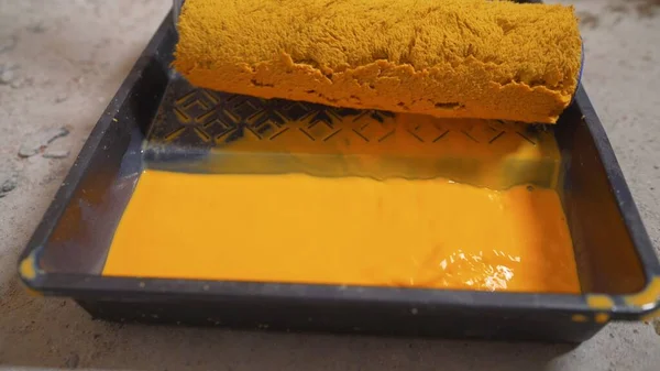 Pour the yellow paint into the tray. A man pours yellow paint into a tray. Yellow paint slowly pours into black paint tray. Wall painting concept. Close-up view.