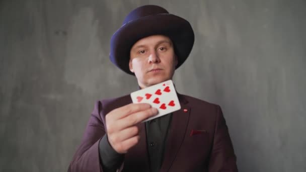 Kouzelník ukazuje trik s hracími kartami. Detailní záběr muže kouzelník se dvěma hracími kartami v ruce přes šedé pozadí. Kouzelník chytře mění hrací karty.