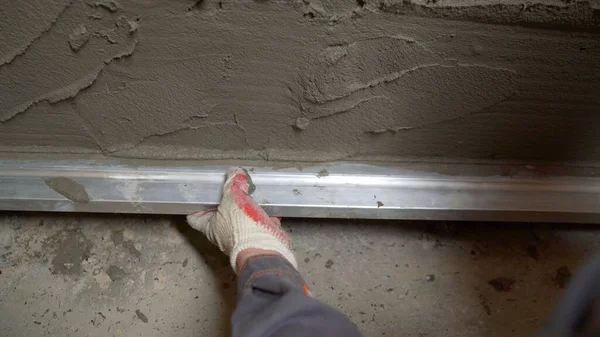 The worker levels the wall using a rule. Builder using shape rule for plastering brick wall.