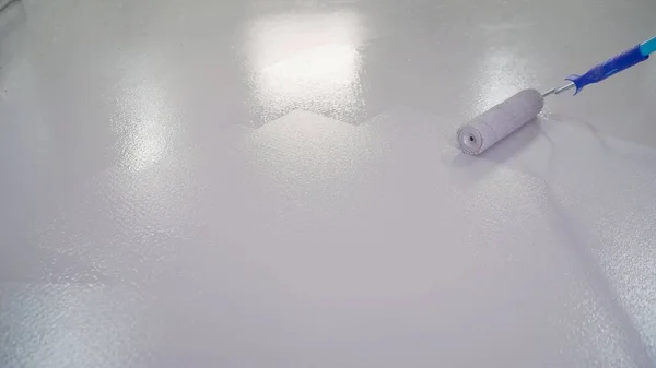 The floor is painted white with a roller. Blue paint roller, on white background. Man painting the floor