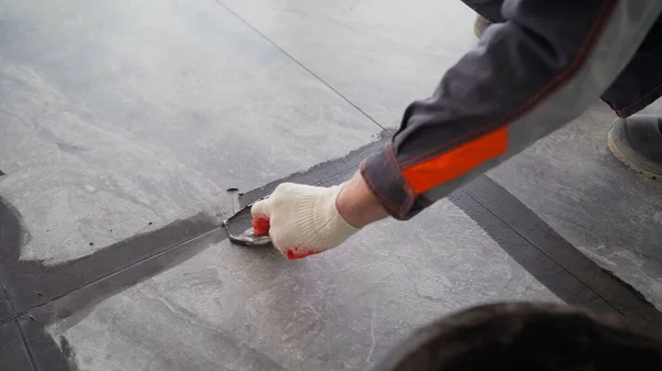 The worker is rubbing the tiles. Black grout tiles on the floor. Close-up of a professional cleaner cleaning the grout with a brush on a gray tiled floor.